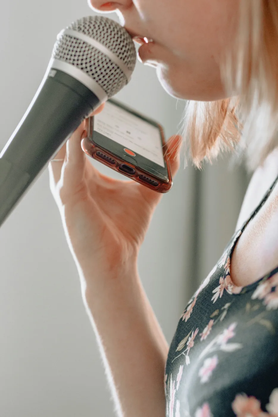 A person recording a voice memo into a phone held next to a handheld microphone